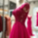 A stunning magenta evening gown adorned with intricate lace detailing, elegantly displayed on a mannequin in an upscale boutique.